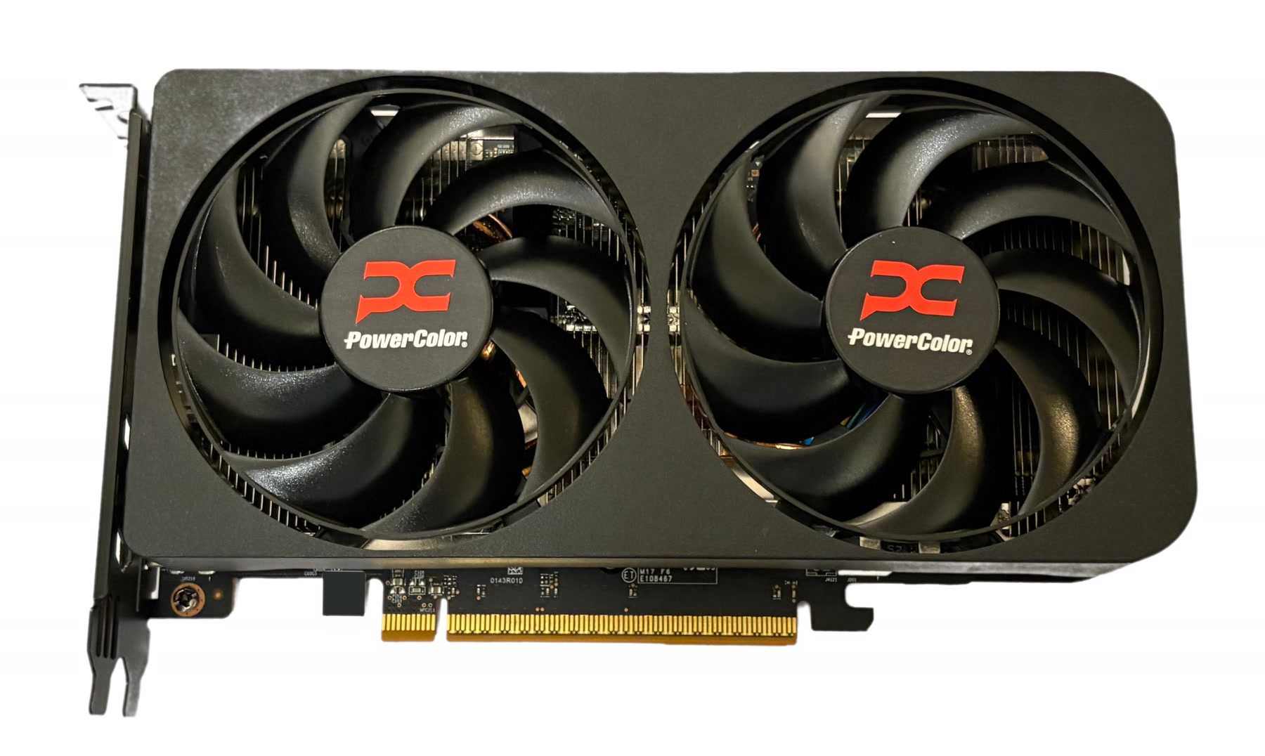 Placa de vídeo preta sobre fundo branco, em vista de três quartos. O cooler tem três ventoinhas com anel prateado. A ventoinha do meio traz a palavra RADEON em branco no miolo. A carcaça é angular, com faixas claras. À esquerda aparece o suporte metálico de encaixe, embaixo os contatos dourados, e à direita a borda da backplate preta com parafusos