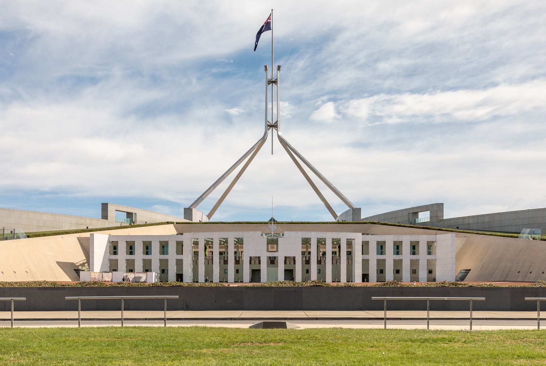 Parliament House em Canberra ao entardecer, com o mastro da bandeira no telhado gramado, o espelho d'água à frente e o céu alaranjado