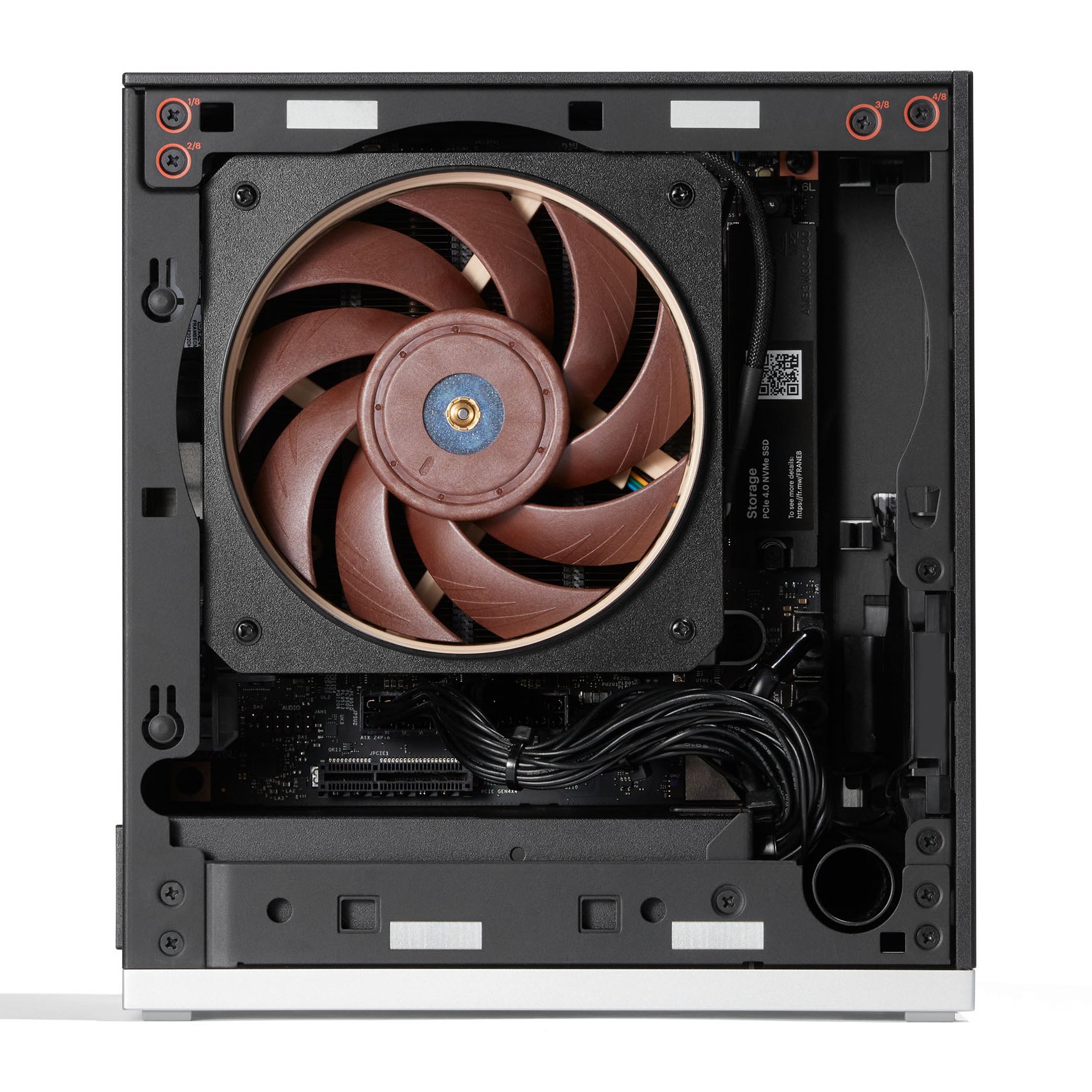 Mini computador de chassi cinza-claro sobre fundo branco. A frente tem um quadrado preto com ventoinha circular de pás escuras e miolo metálico. O logotipo Framework fica no canto inferior esquerdo da frente. A lateral direita é uma malha perfurada. A tampa de cima é escura