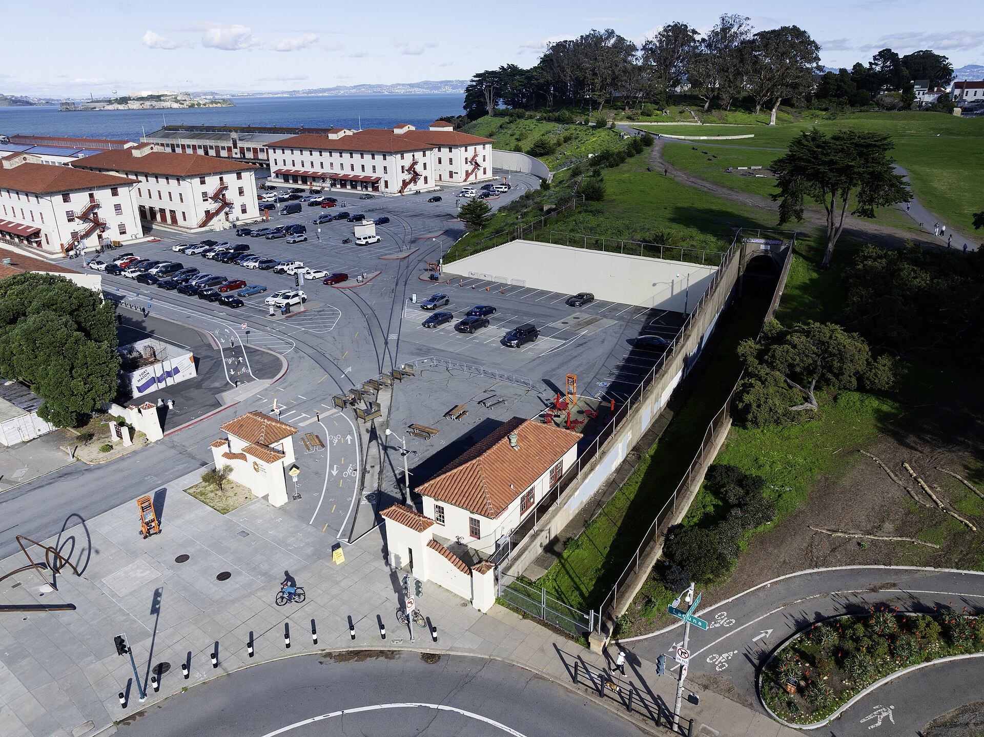 Fachada de tijolos vermelhos sob céu azul, com uma faixa horizontal clara. Na faixa, letras escuras grandes formam FORT MASON CENTER e, abaixo, letras menores formam FOR THE ARTS. Há janelas brancas de várias folhas dos dois lados da faixa, arbustos verdes na base e chão de concreto